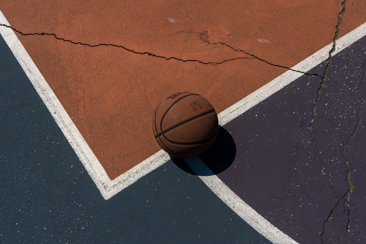 A basketball resting on a cracked outdoor court surface