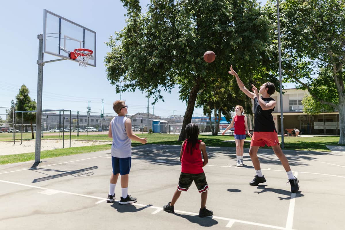 A group of children playing basketball on a sunny outdoor court with trees around