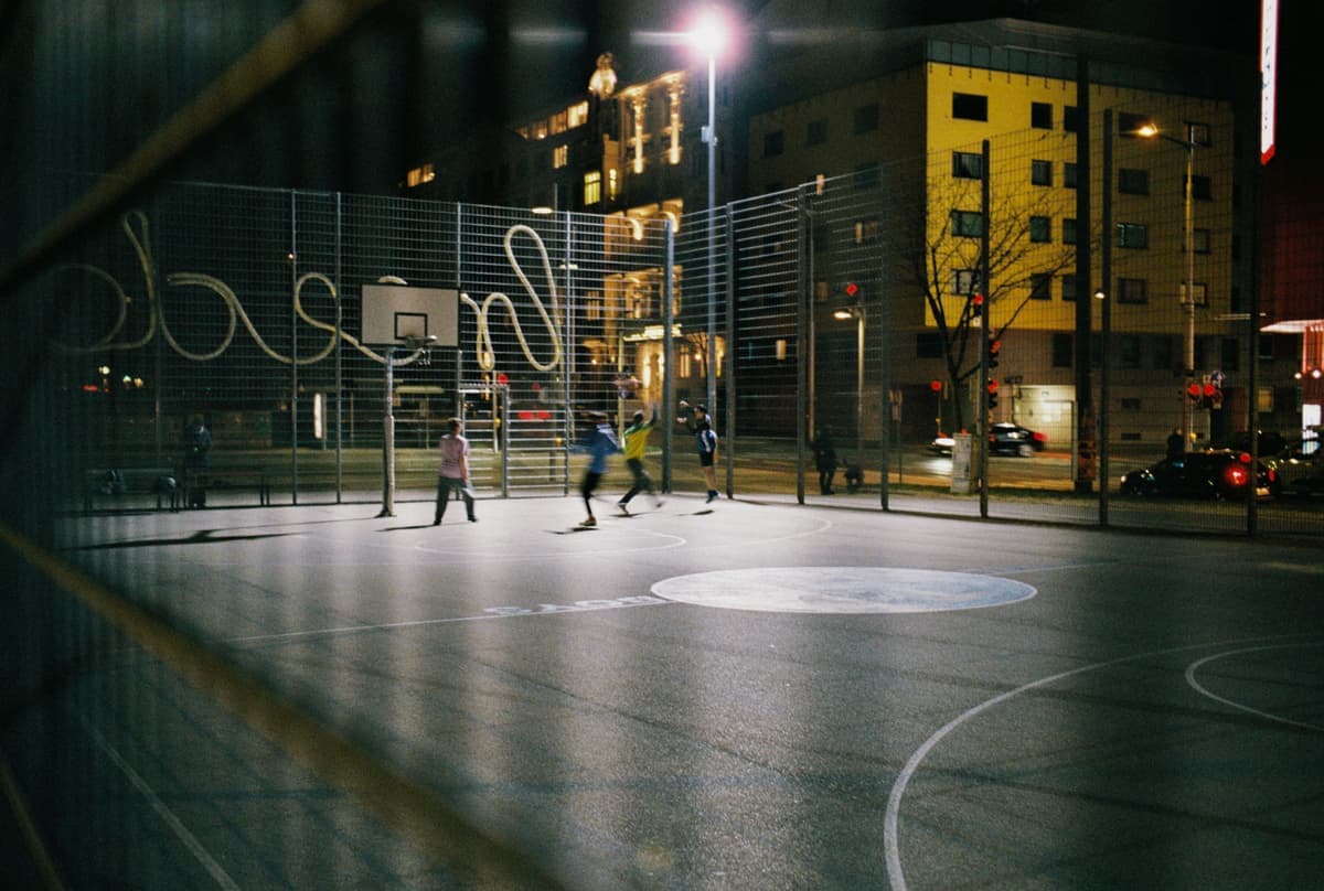 People playing basketball on a lit outdoor court at night