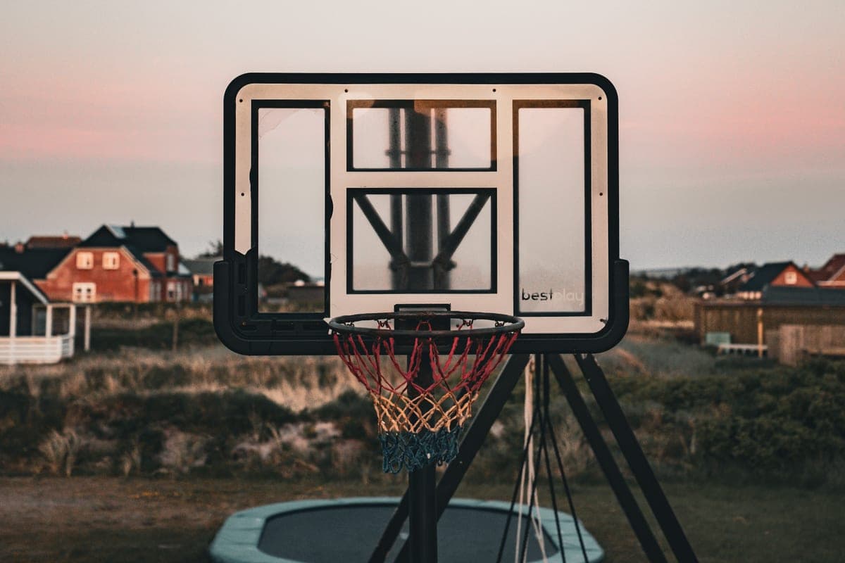 An outdoor basketball hoop with a colorful net against a sunset sky