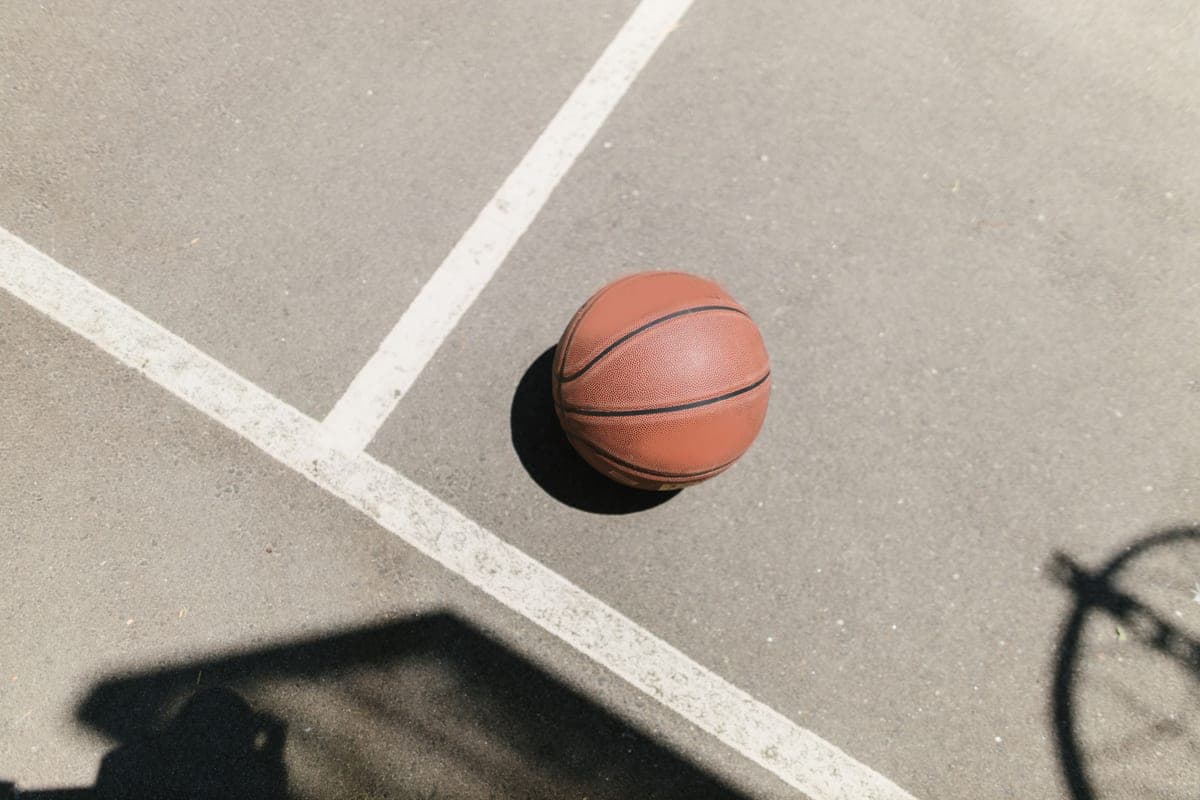 A basketball resting on a sunlit concrete court with the shadow of a hoop
