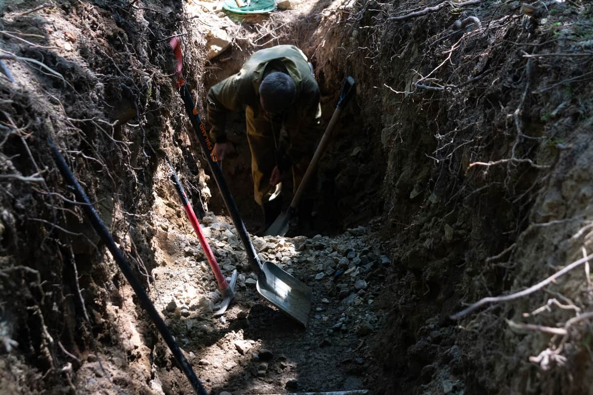A person digging a hole outdoors with shovels and tools nearby